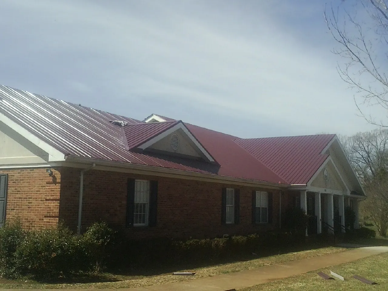 Red metal roof with gabled entries on a long brick building, from a Hail Damage Roof Repair job in Saint Helena Island