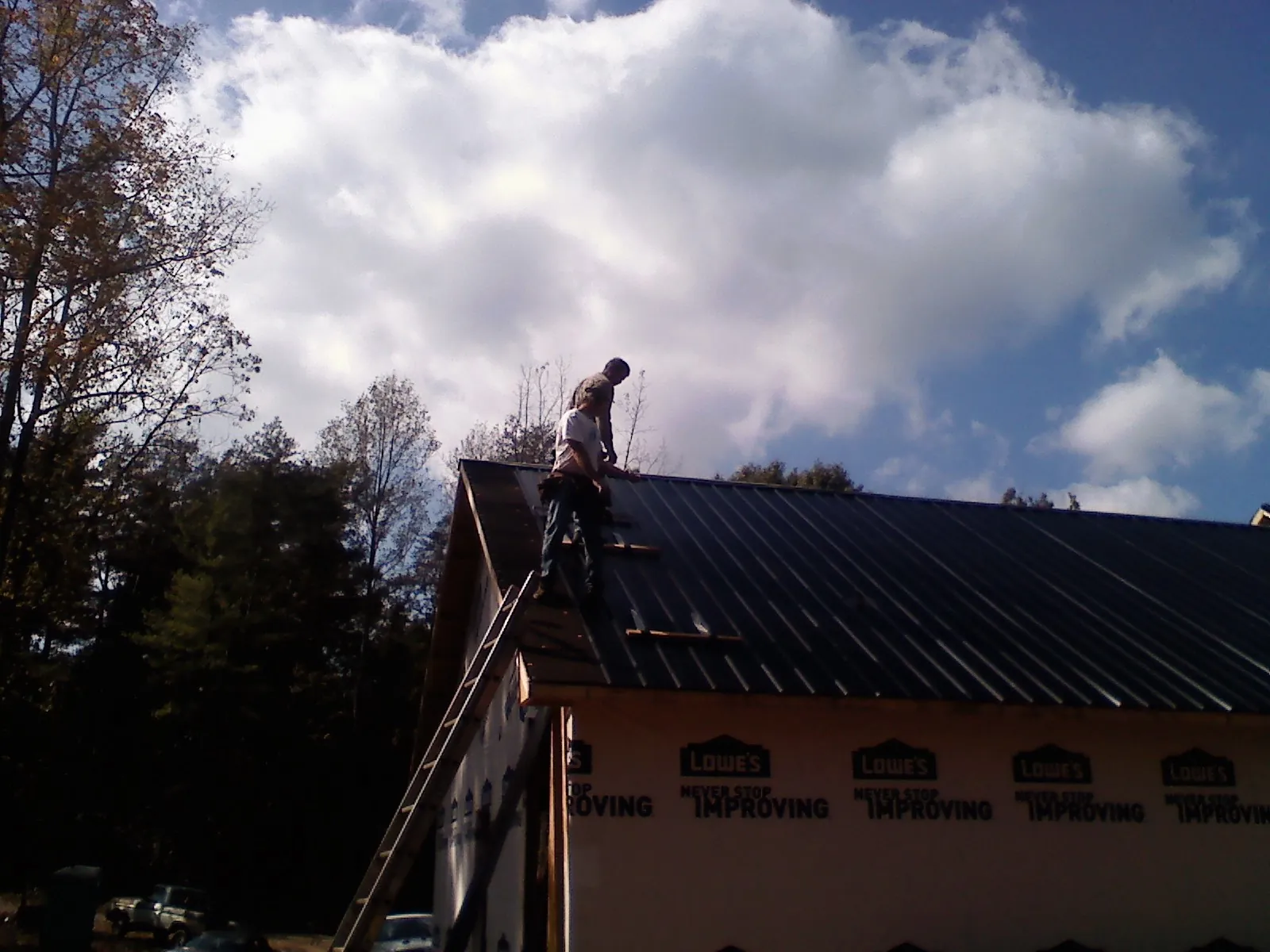 Roofer fastening dark metal panels high against a cloudy sky, from a Roof Inspection job in Saint Helena Island