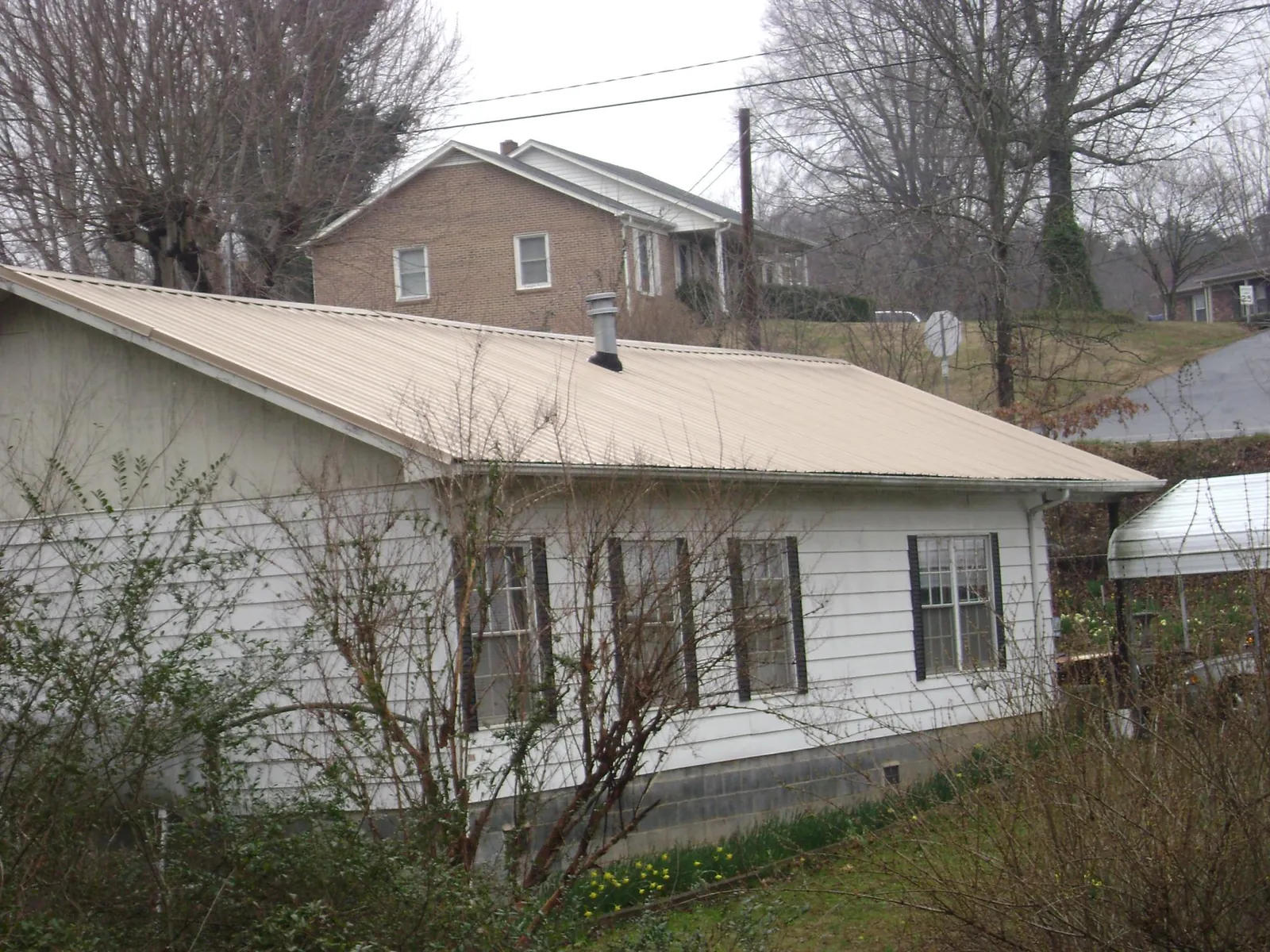 Tan metal roof on a white sided house set into a hillside — Commercial Roofing by Roofing Brothers in Saint Helena Island